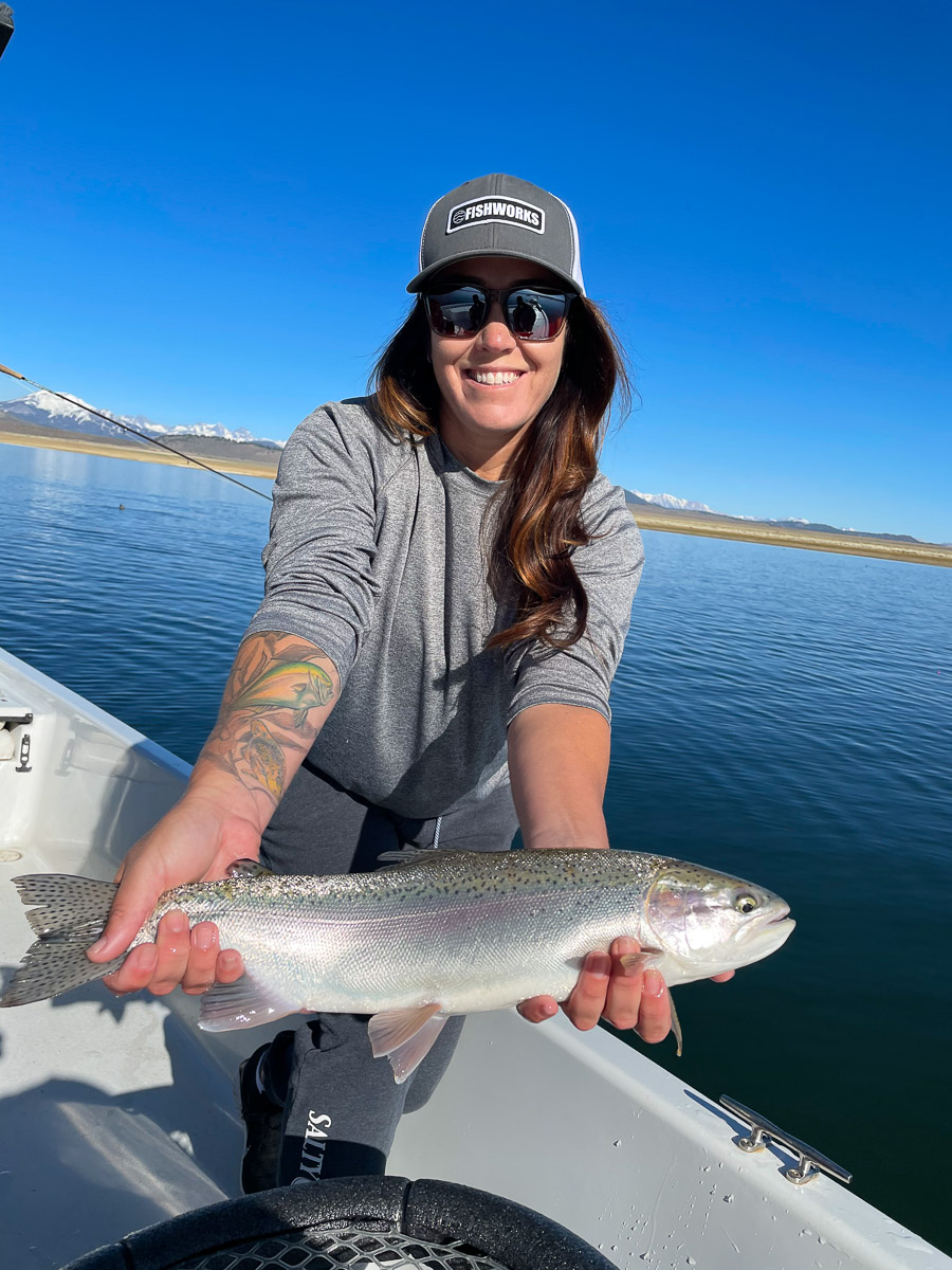 A female fly fisher holding a giant rainbow trout in a boat on Crowley Lake.