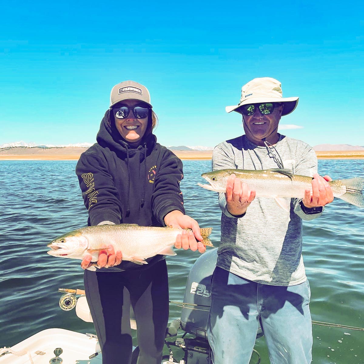  A male and female fly fisher pair holding a pair of rainbow trout on a lake.