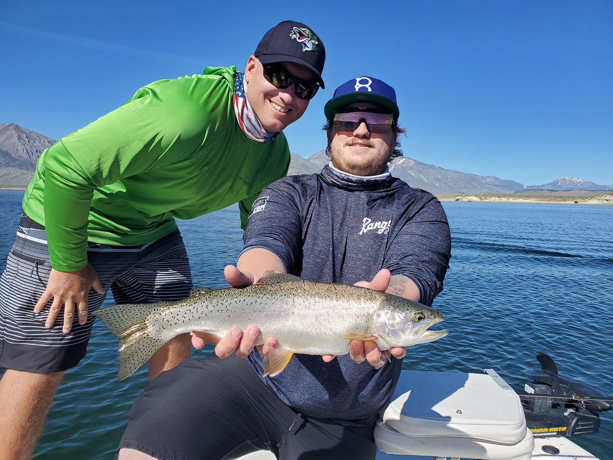 A smiling fly fisherman holding a cutthroat trout on a lake in a boat.