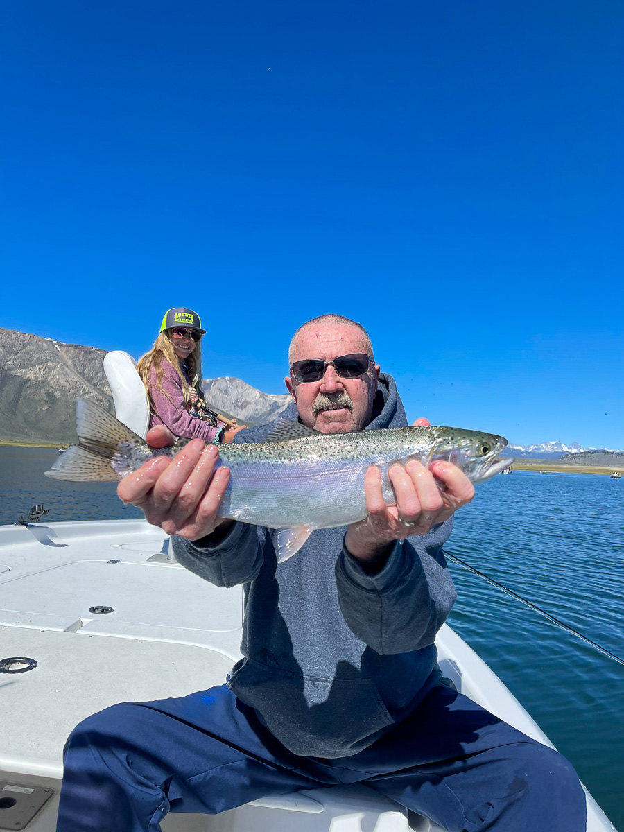 A fly fisheman holding a big rainbow trout in a boat on a lake.