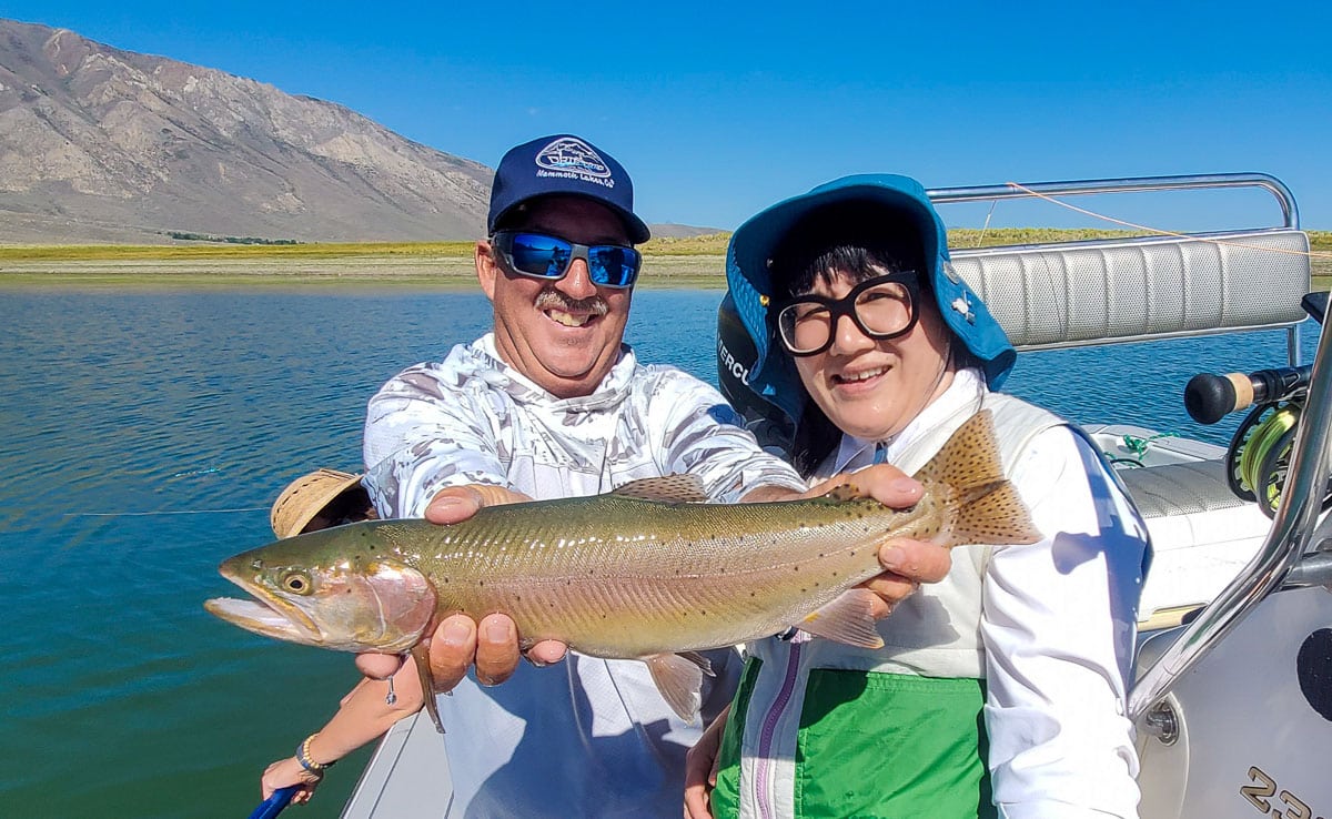 A smiling fly fisherman holding a cutthroat trout on a lake in a boat.