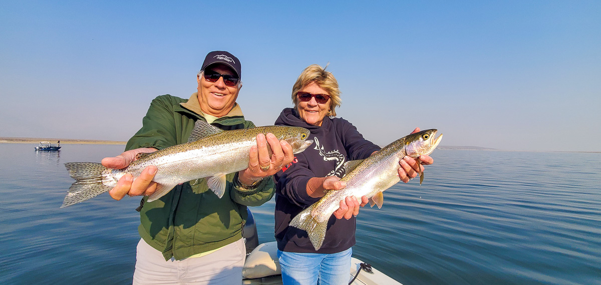 A man and a woman holding a pair of larger rainbow trout while on a lake.