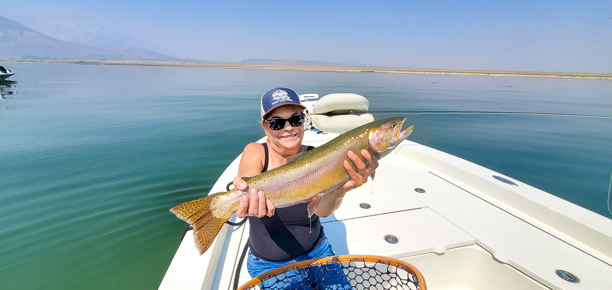 A female angler holding a giant cutthroat trout on a lake in a boat.