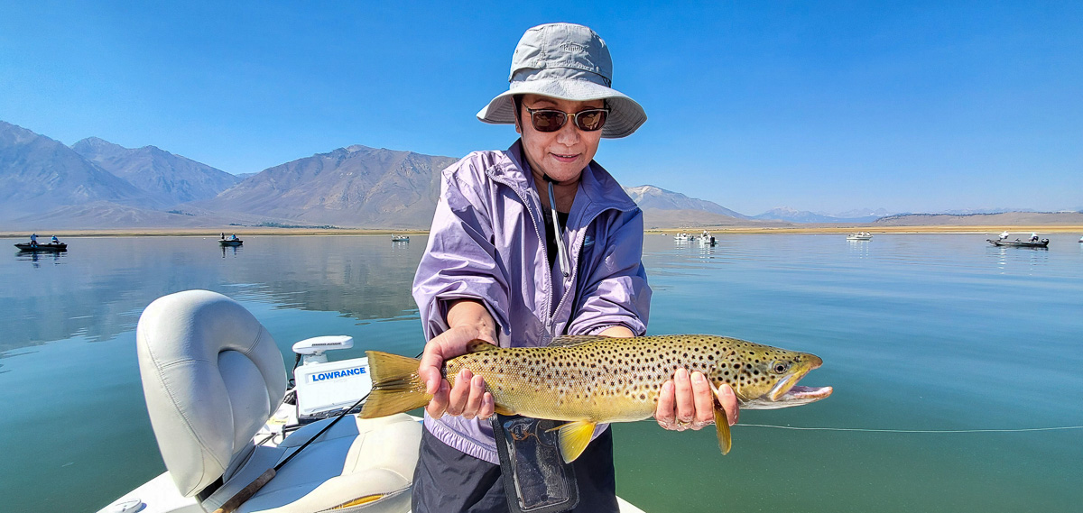 A female angler holding a giant cutthroat trout on a lake in a boat.