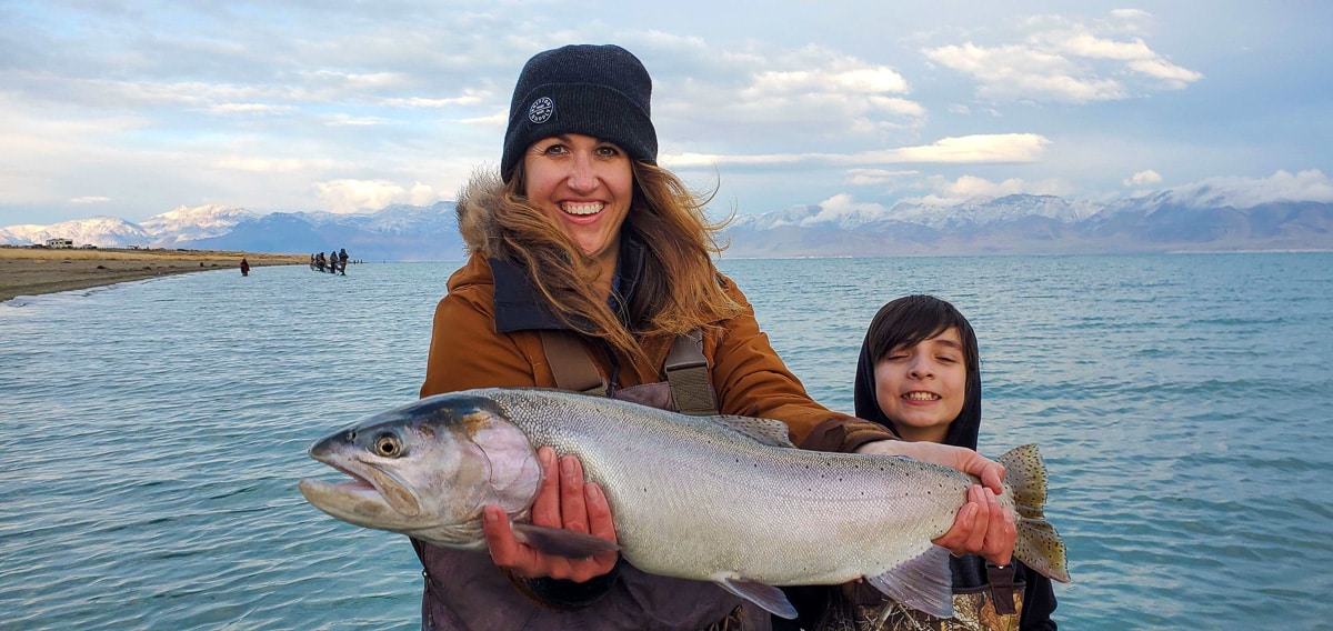 A fly fisherman holding a giant cutthroat trout on a lake.