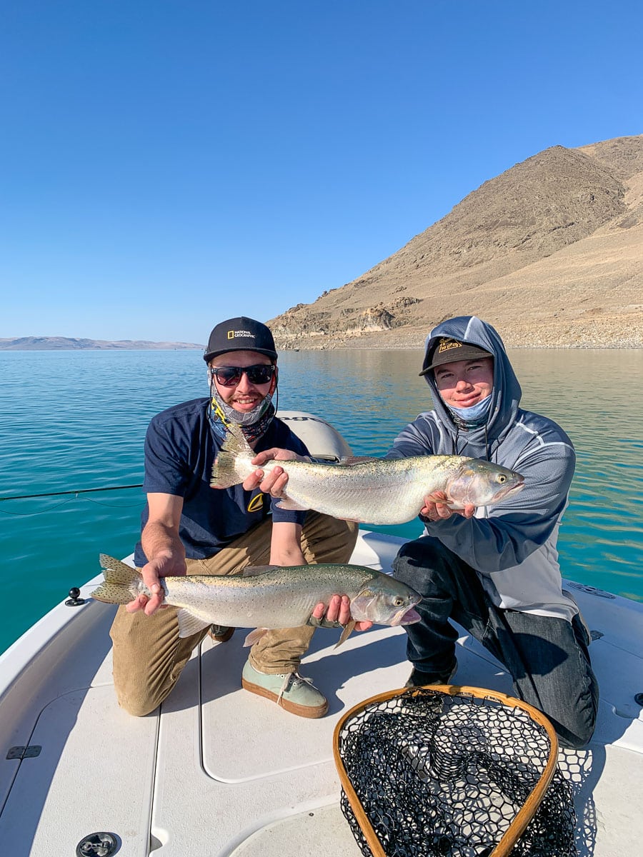 A fly fisherman holding a giant cutthroat trout on a lake.