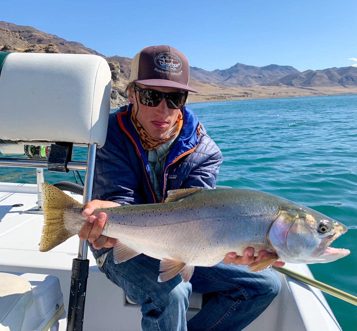 A fly fisherman holding a giant cutthroat trout on a lake.