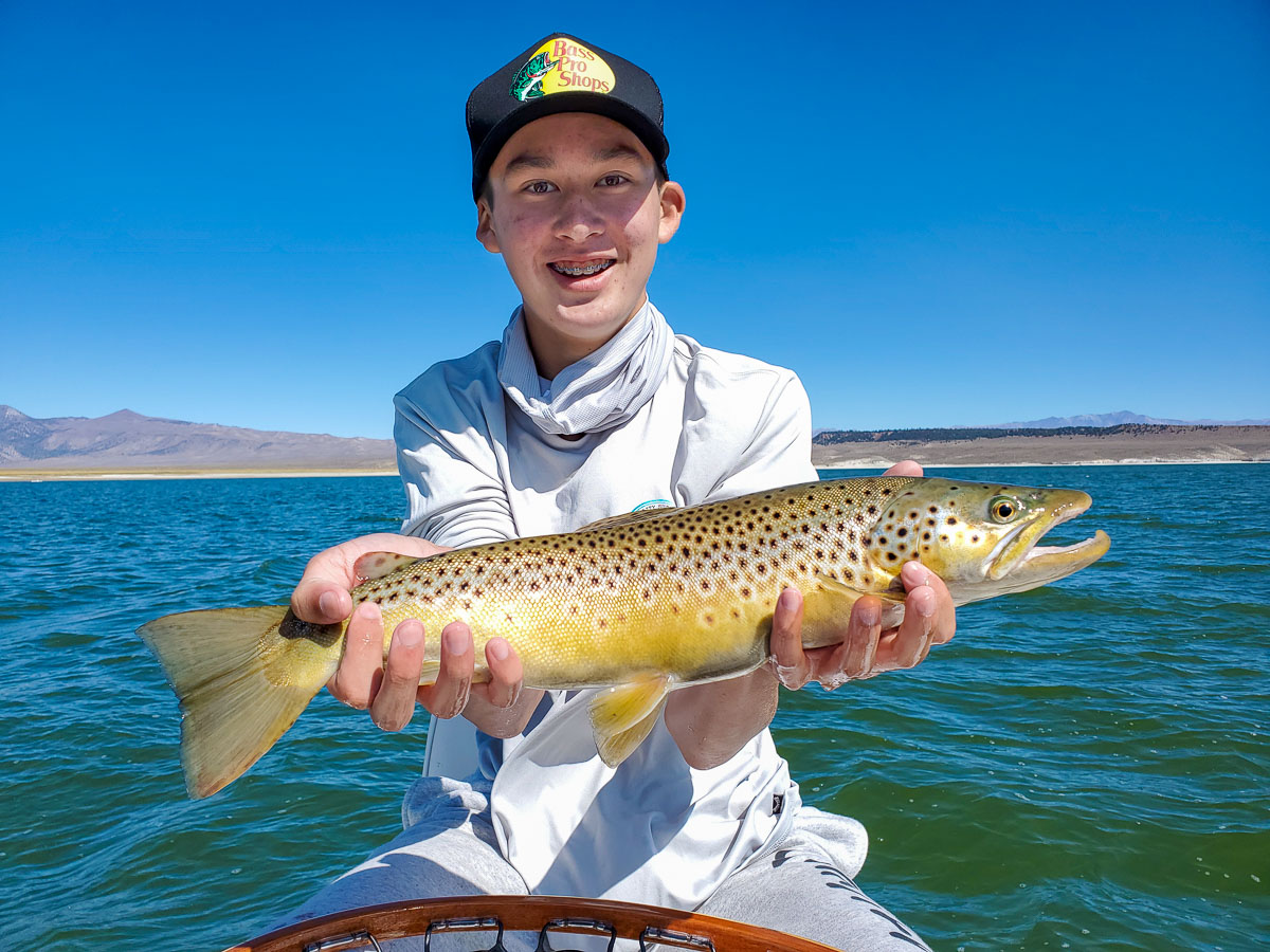 A young fly fisherman holding a nice brown trout on a lake with waves.