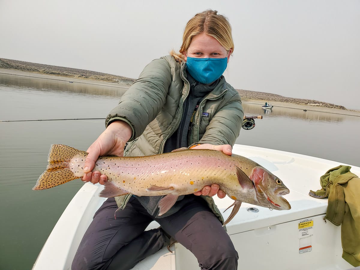 A lady angler holding a nice cutthroat trout in a boat on a lake.