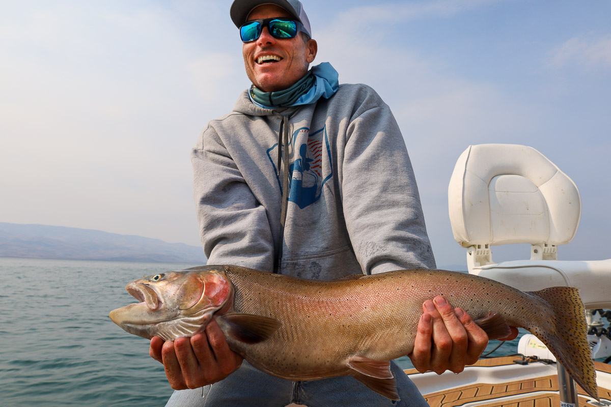 An angler holding a giant cutthroat trout on a lake in a boat.