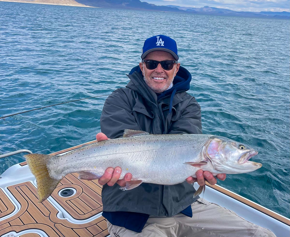 A fly fisherman on a lake in a boat holding a behemoth cutthroat trout.