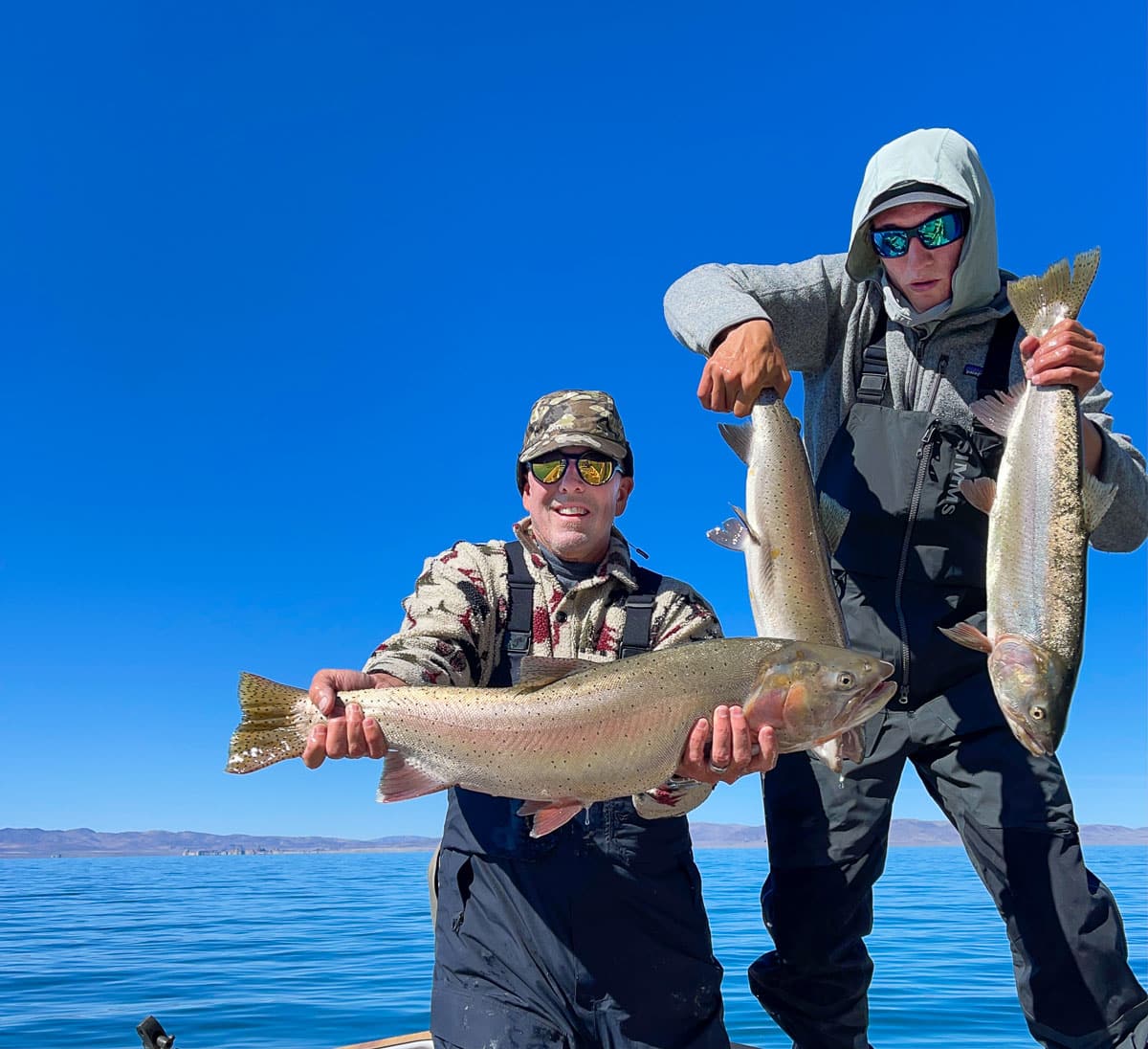 A couple of fly fishermen holding a pair of trout on a lake.