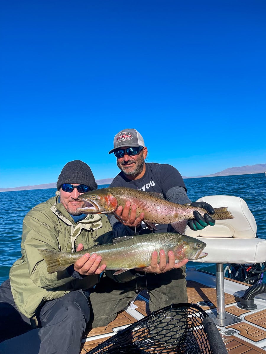 A couple of fly fishermen holding a pair of trout on a lake.