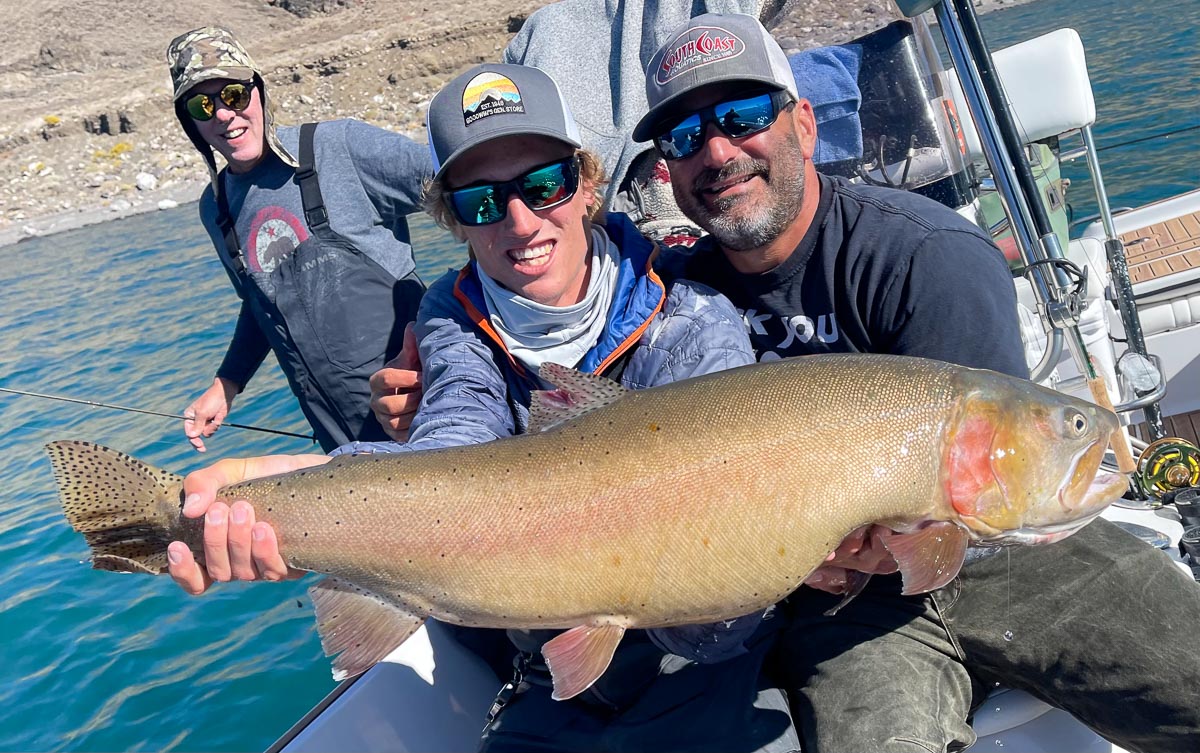 A fly fisherman on a lake in a boat holding a behemoth cutthroat trout.