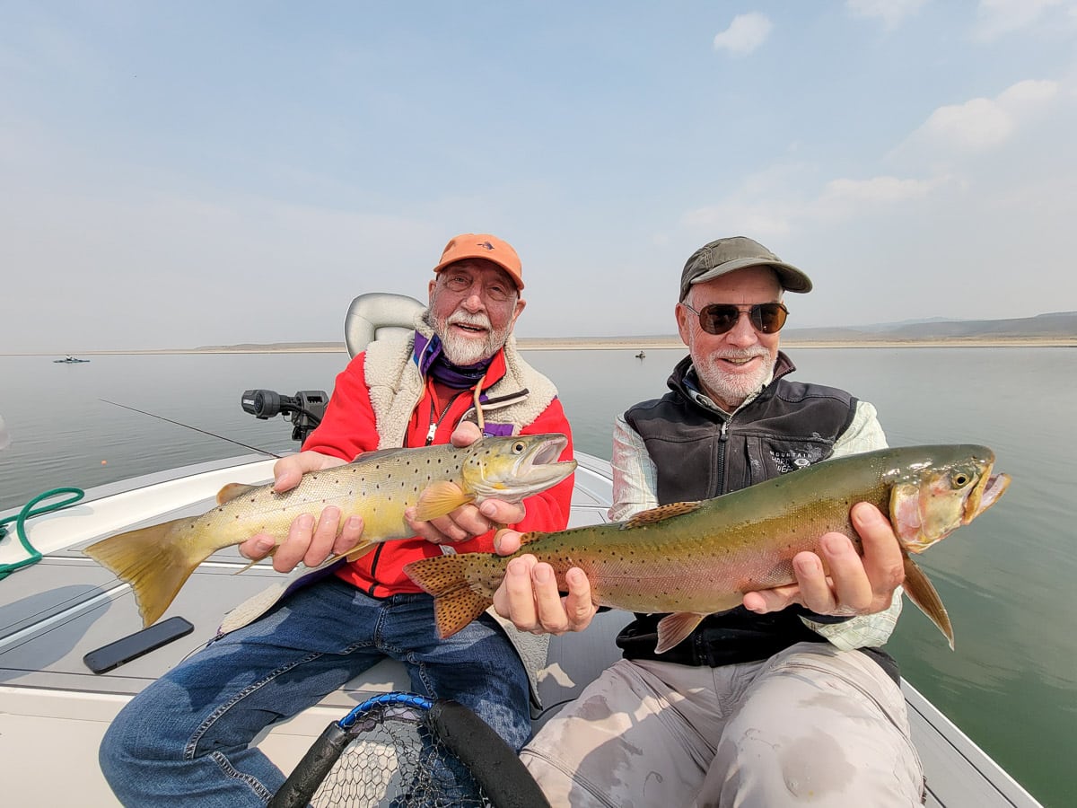 A couple of fly fishermen holding a pair of trout on a lake.