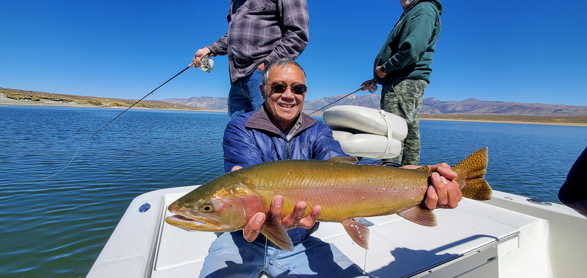 A fly angler holding a giant cutthroat trout on a lake in a boat.