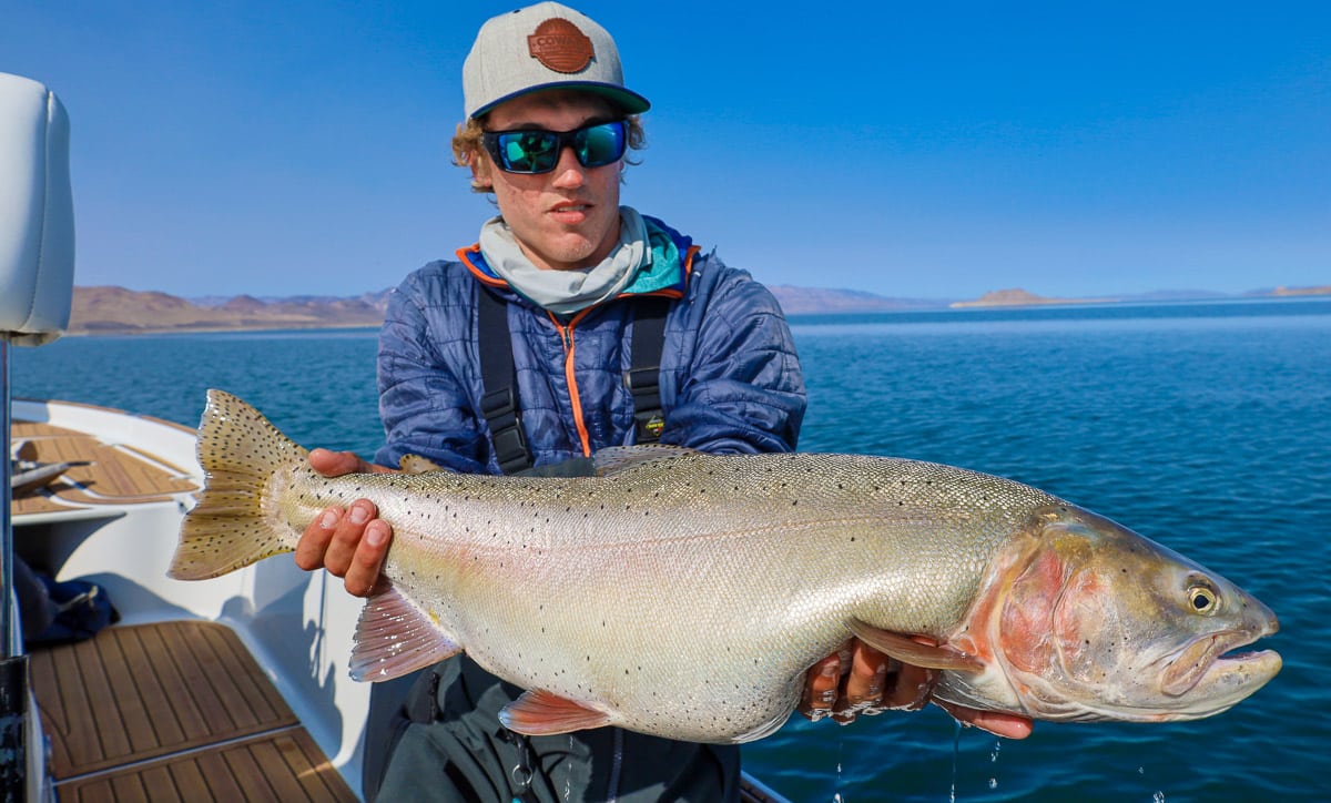 A fly fisherman holding a massive cutthroat trout on a lake.