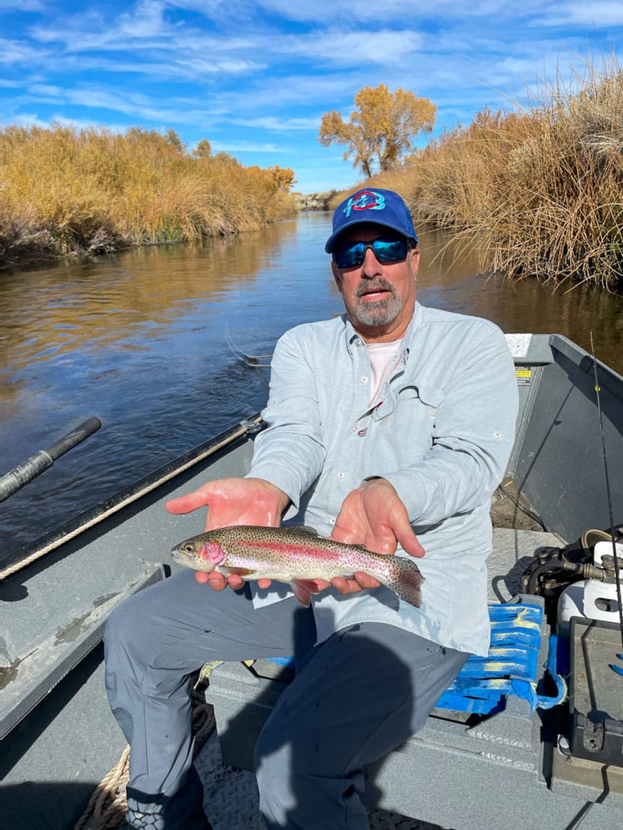 An angler holding a giant cutthroat trout on a lake in a boat.