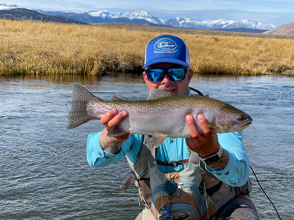 A smiling fly fisherman holding a brown trout on a river.