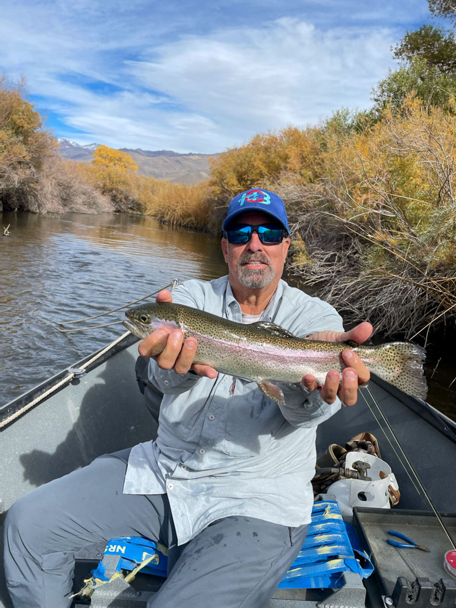 A smiling fly fisherman holding a brown trout on a lake in a boat.