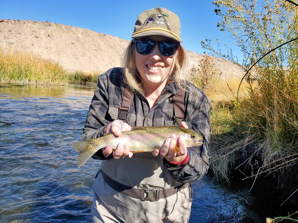 A fly fisherman on a lake in a boat holding a behemoth cutthroat trout.