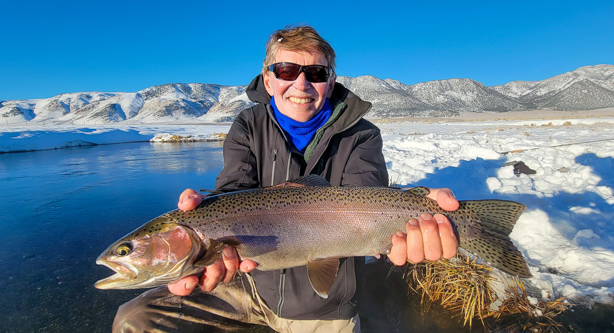 A smiling fly fisherman holding a rainbow trout on a river.