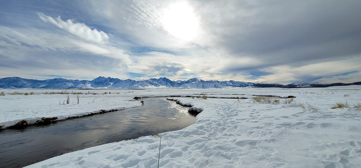 A meandering river during with snow on the ground and snow filled mountains.