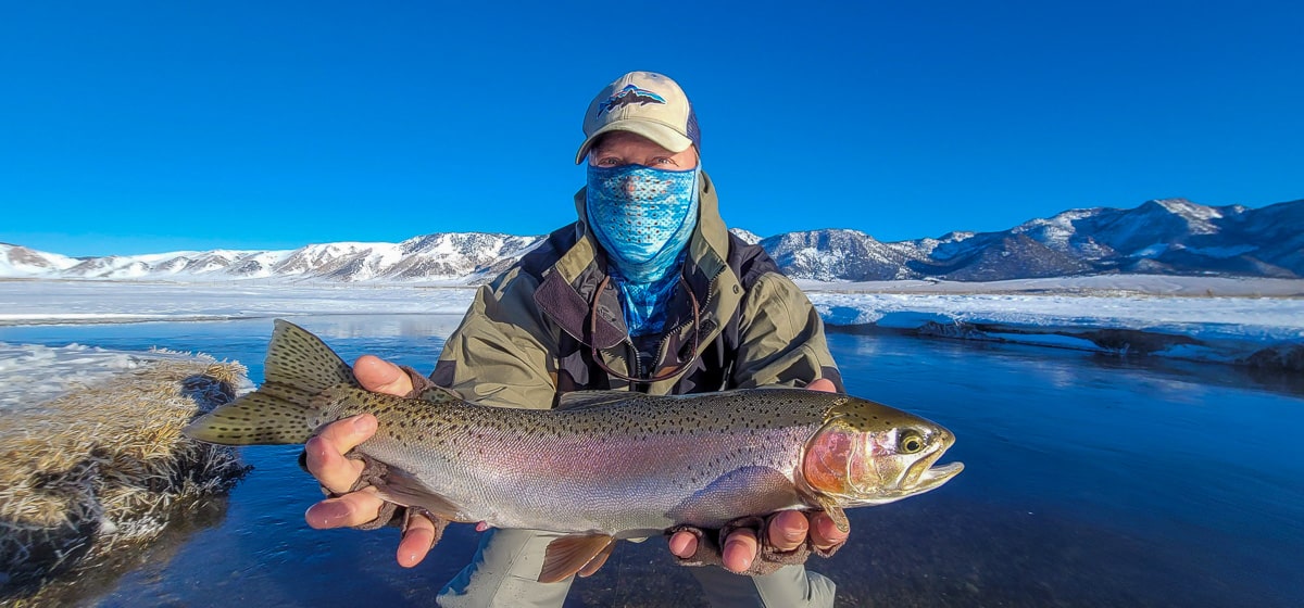 A smiling angler holding a giant rainbow trout on a river.