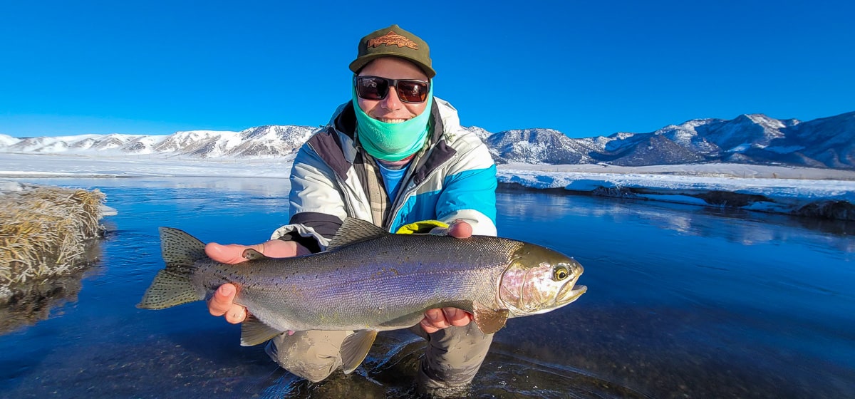 A smiling fly fisherman holding a rainbow trout on a river.