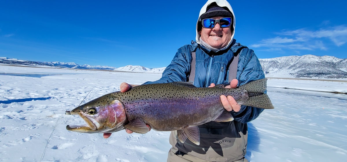 A smiling fly fisherman holding a rainbow trout on a river.