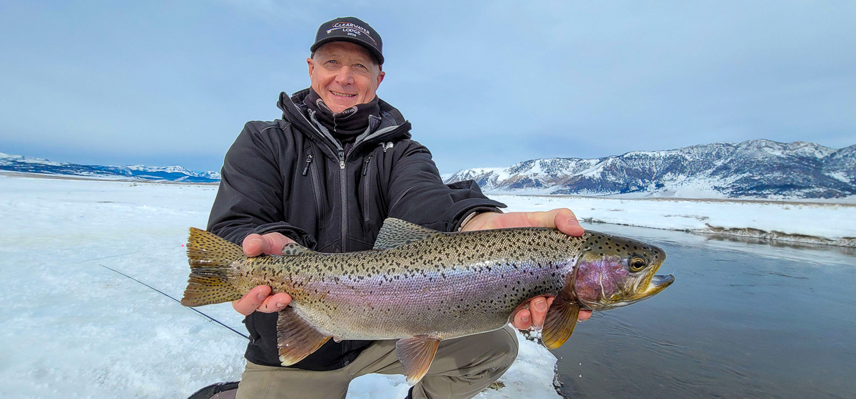 A smiling fly fisherman holding a rainbow trout on a river.