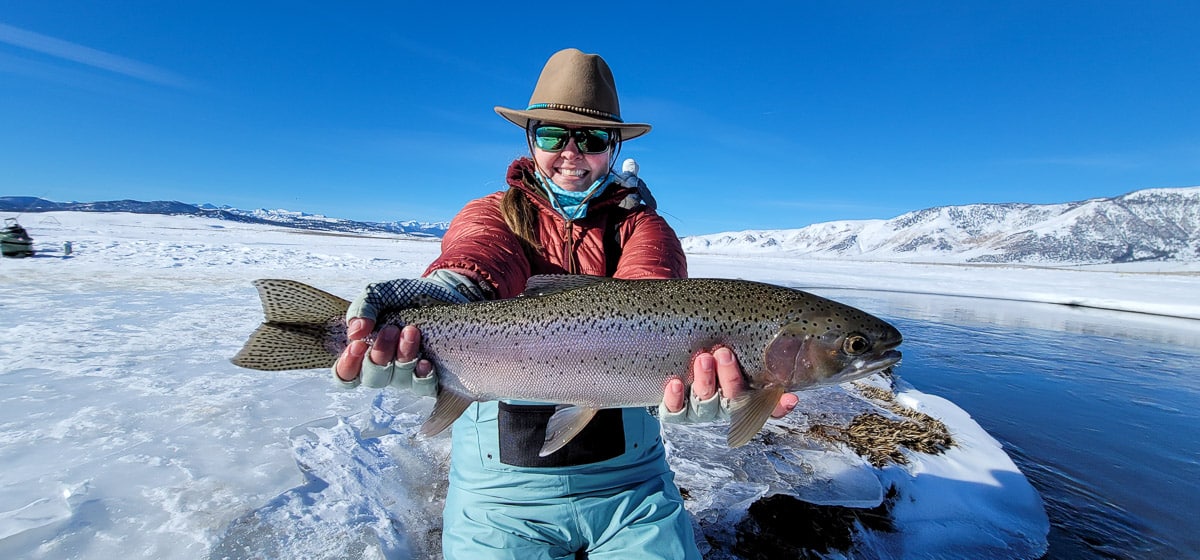 A smiling fly fisherman holding a rainbow trout on a river.