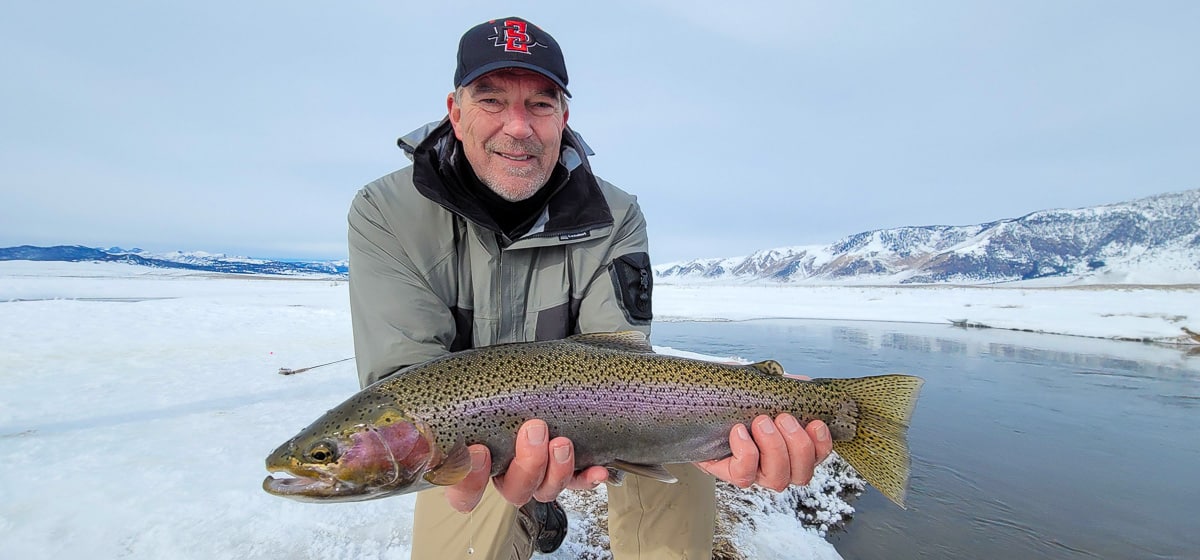 A smiling fly fisherman holding a rainbow trout on a river.