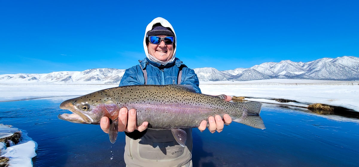 A smiling fly fisherman holding a rainbow trout on a river.