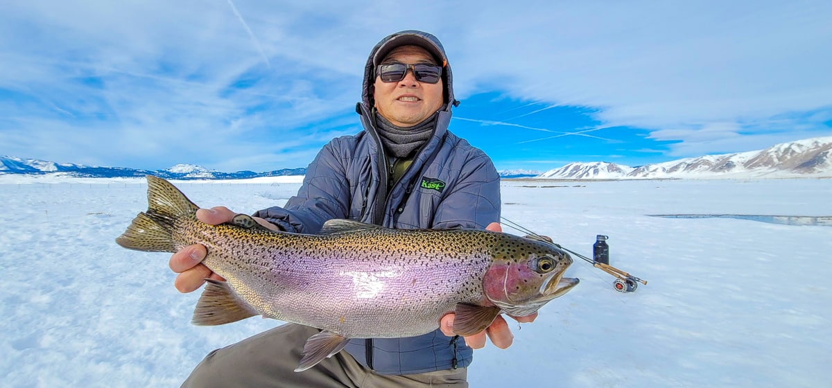 A smiling fly fisherman holding a rainbow trout on a river.