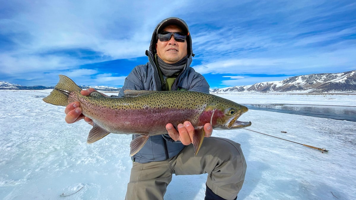 A smiling fly fisherman holding a rainbow trout on a river.