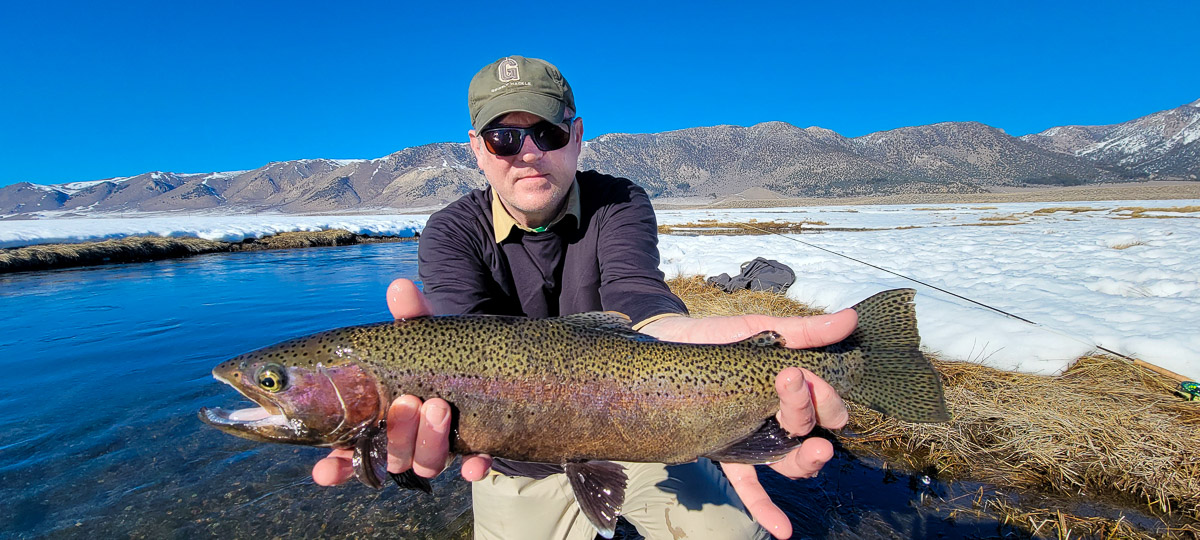 A man holding a large rainbow trout in the snow.