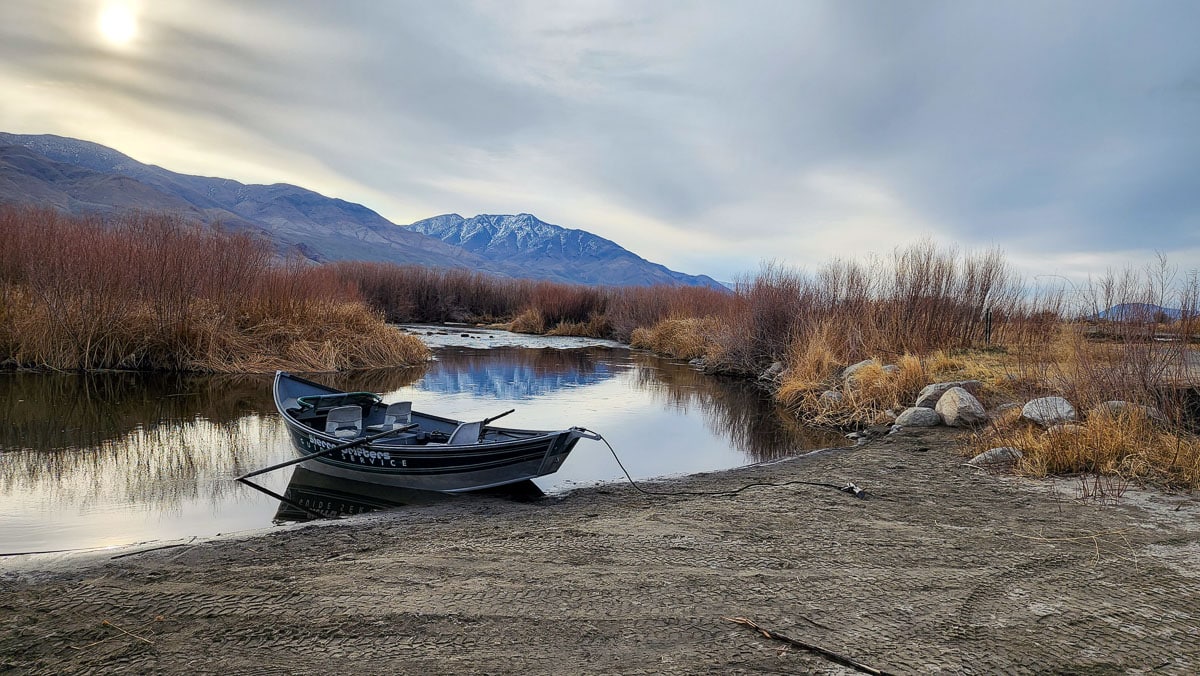 A row boat beach along the bank of a river on a cloudy day.