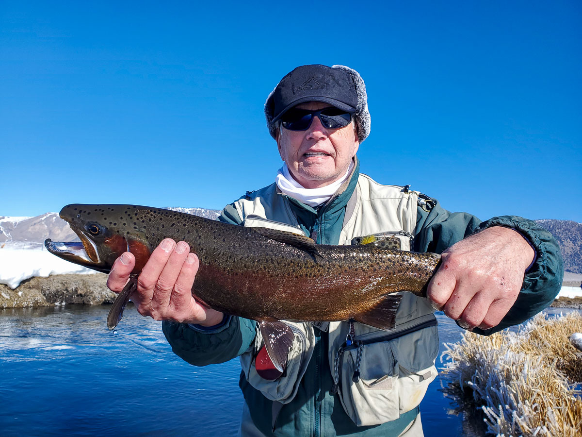 A smiling female angler holding a giant rainbow trout on a river.