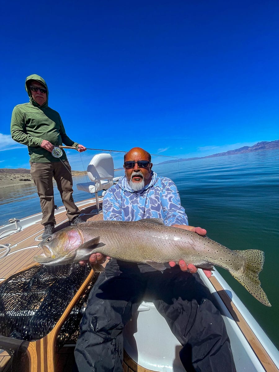 A fly fisherman on a lake in a boat holding a behemoth cutthroat trout.