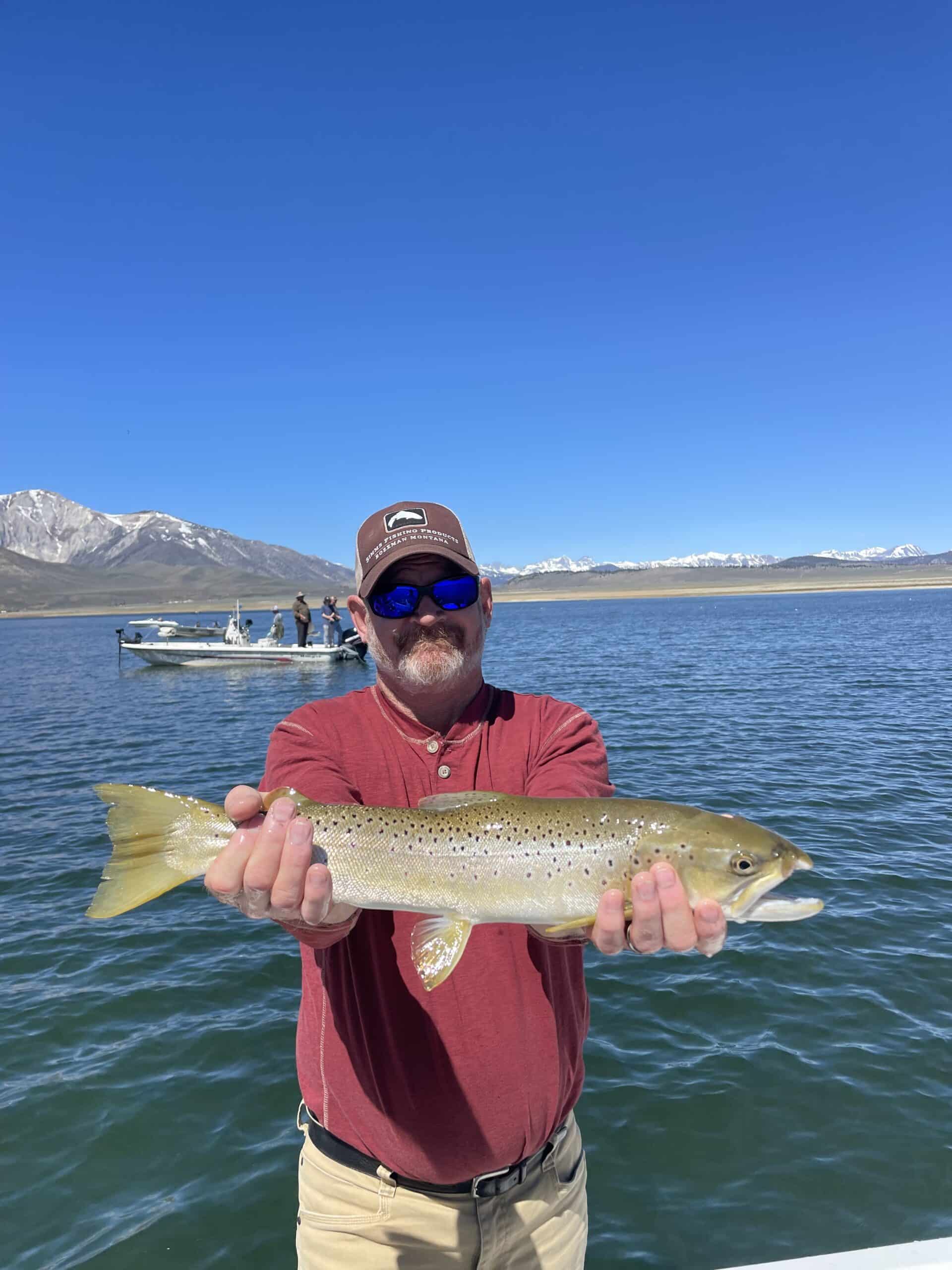 A fly fisherman on a lake in a boat holding a behemoth brown trout.