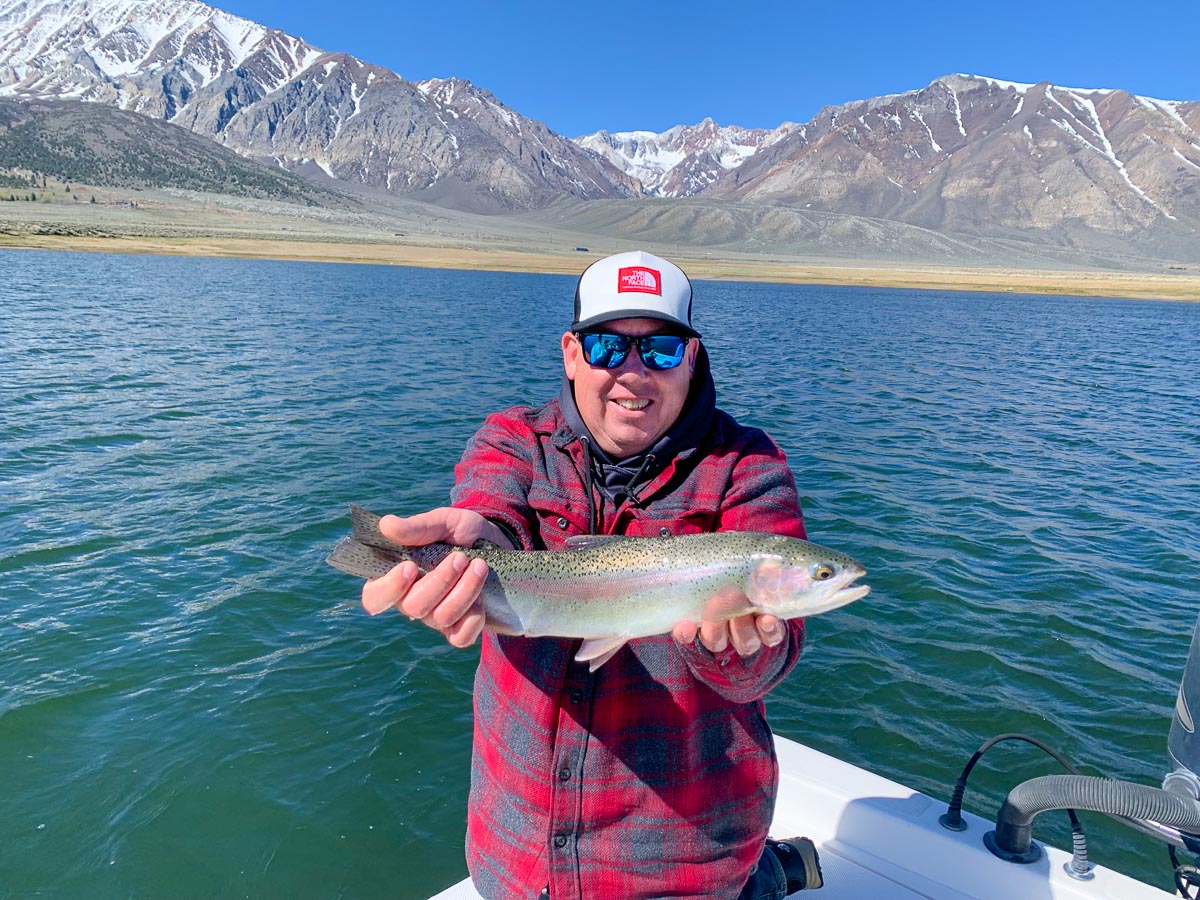 A pair of fishermen in a boat on a lake holding a pair of large cutthroat trout.