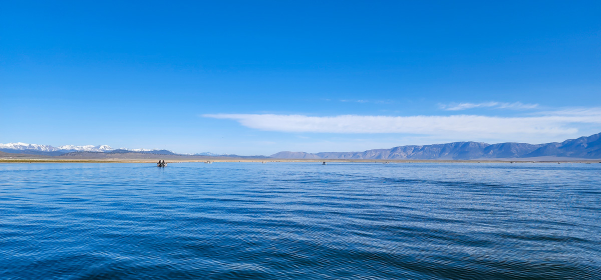 A large lake with snowy mountains in far off in the background and a couple boats on the water.