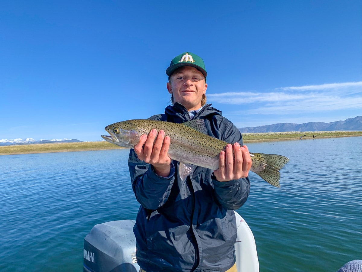 A fly fisherman on a lake in a boat holding a behemoth rainbow trout.