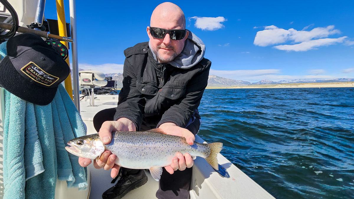 A fly fisherman on a lake in a boat holding a behemoth rainbow trout.