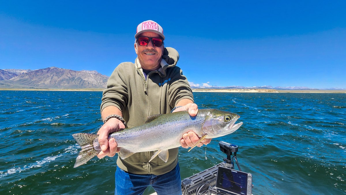 A fly fisherman on a lake in a boat holding a behemoth rainbow trout.