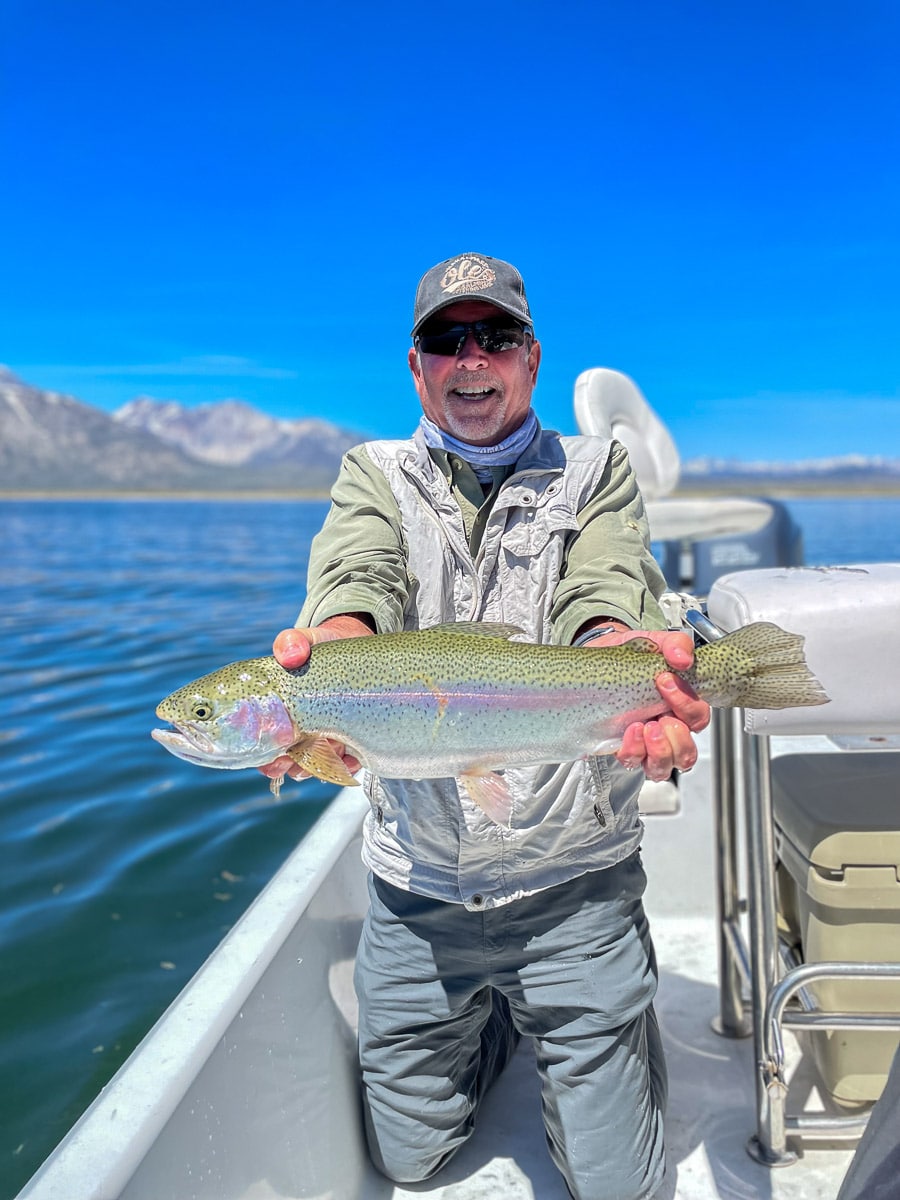 A fly fisherman on a lake in a boat holding a behemoth rainbow trout.