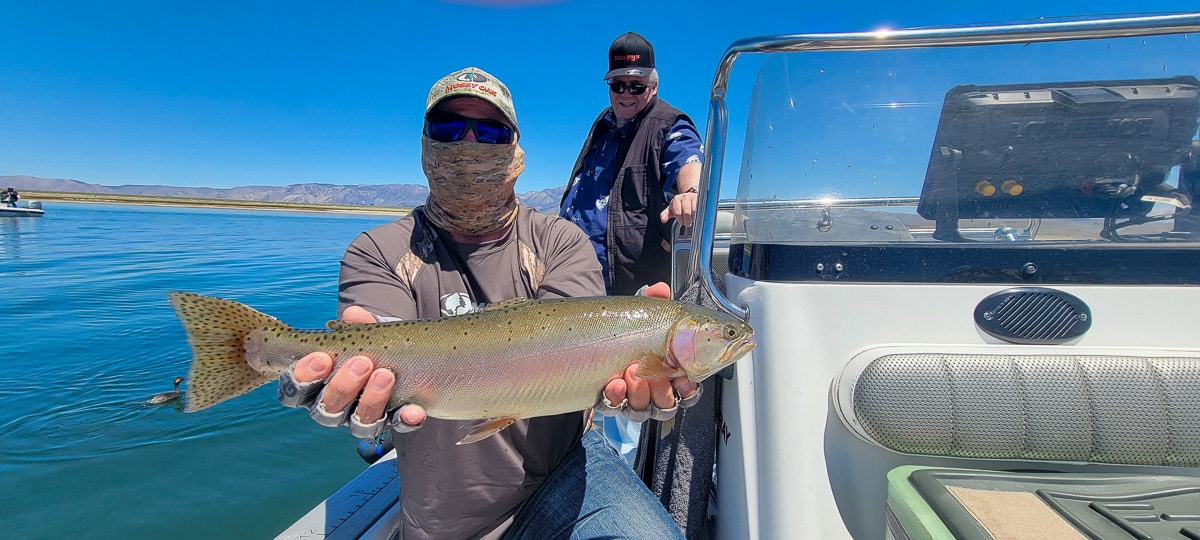 A fly fisherman in a boat holding a large cutthroat trout.