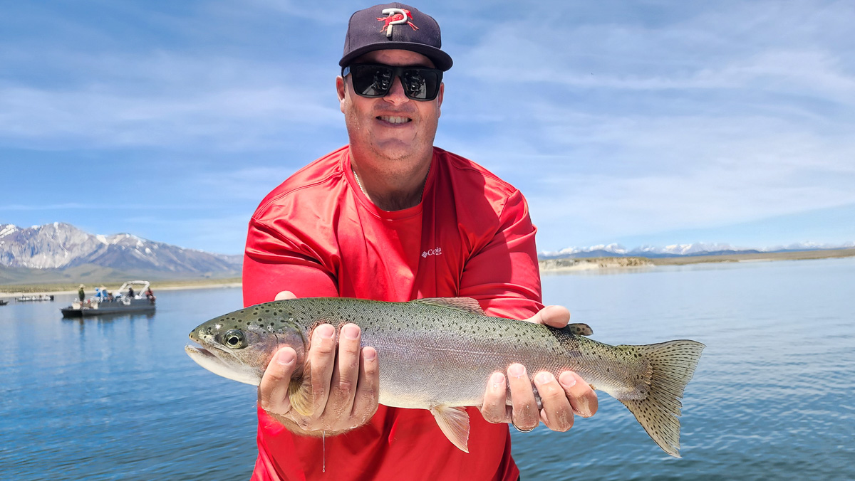 A fly fisherman holding a large cutthroat trout on a lake.