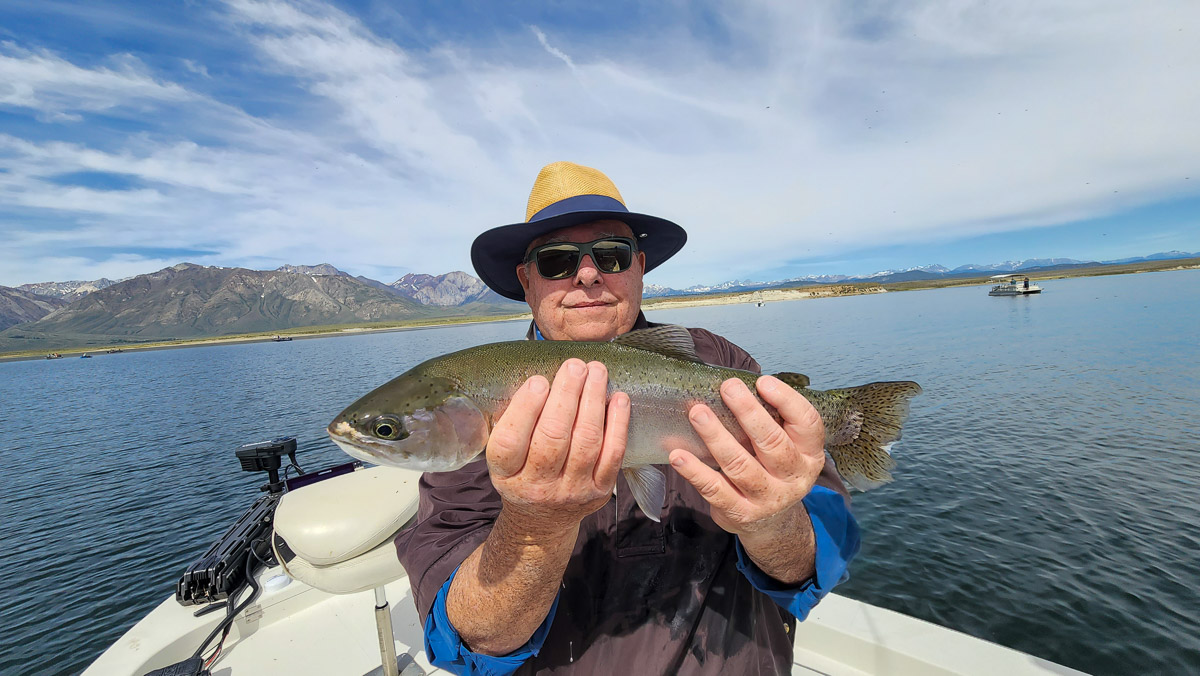 A fisherman holding a giant rainbow trout on a lake.